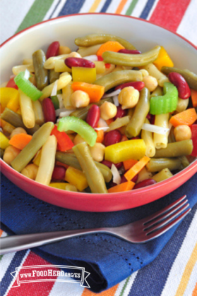 Se muestra un tazón de ensalada elaborada con distintos tipos de frijoles y verduras crujientes sobre un mantel a rayas.