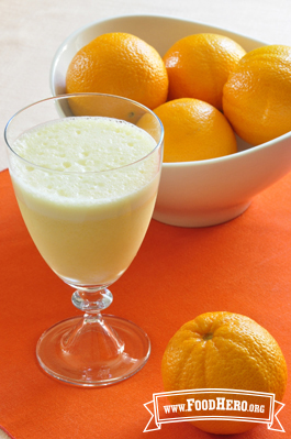 Footed glass filled with a frothy orange juice drink.