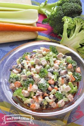 Chopped broccoli, mixed with vegetables, chopped nuts and dressing, is displayed in a serving bowl.