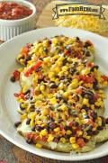 Platter of potatoes stuffed with beans, corn, salsa and sprinkled with melted cheese.