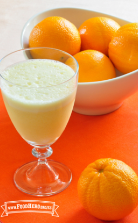 Vaso con pie lleno con una bebida espumosa de jugo de naranja.