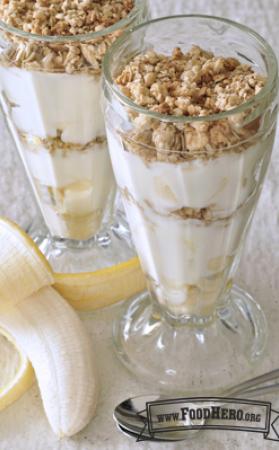 Glass cups with layers of yogurt, banana and granola. 