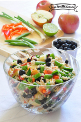 Un recipiente transparente muestra una colorida ensalada de cebada cocida, arándanos azules y verduras crujientes.
