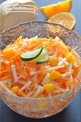 Rodajas crujientes de jícama y zanahoria con naranjas adornadas con limón verde en un recipiente de vidrio.