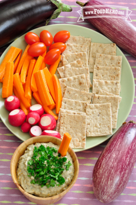 Eggplant dip garnished with parsley served with a vegetable and cracker plate.