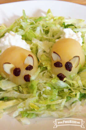 Peeled pear on a lettuce bed with almonds, cottage cheese and raisins appearing like a bunny.