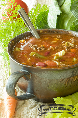 Bowl of soup with a tomato base, vegetables and ground meat.