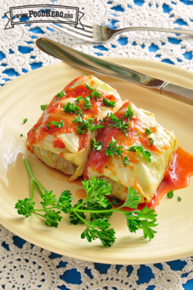 Two tightly wrapped cabbage rolls covered in tomato sauce with a parsley garnish.