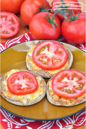 Plato con mitades de panecillos ingleses con queso y una rodaja de tomate.