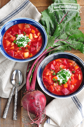Bowls of vibrant red beet and vegetable soup with a dollop of sour cream and parsley.  