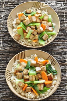 Marinated tofu cubes are baked and combined with stir-fry vegetables and shown over bowls of brown rice.