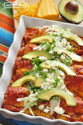 Baking dish of enchiladas served with avocado, lettuce and cheese down the center.