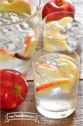 Se muestran vasos de refrescante Agua con Sabor a Manzana y Canela con guarnición de rodajas de manzana.