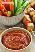 Se muestra un tazón de salsa de plátano y jengibre con tiras de verduras crudas y brochetas de tofu a la parrilla.
