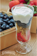 Un vaso de helado lleno de capas de fresas rebanadas, granola, arándanos azules y yogur cremoso.