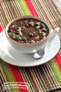 Un tazón de sopa caliente con frijoles negros y verduras, adornado con hierbas.