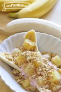 A bowl with halved banana is topped with yogurt, pineapple chunks and a sprinkle of granola.