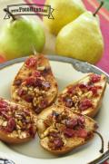 Four pear halves stuffed with walnuts and cranberries sprinkled with cinnamon in a bowl.