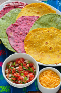 Tortillas de colores brillantes servidas junto con queso rallado y salsa.