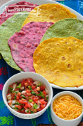 Yellow, red and green tortillas on a platter with salsa and grated cheese on the side.