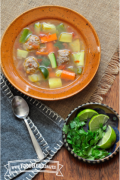 Tazón de sopa de albóndigas, arroz y verduras con limón verde y cilantro.