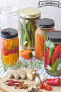 Glass jars of peppers, garlic, asparagus and carrots in pickling brine. 