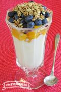 Glass cup with layers of yogurt, peach, blueberries and granola.