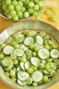 Thinly sliced cucumber and grape halves with dressing in a bowl.