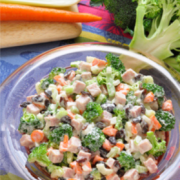 Brócoli picado, mezclado con verduras, nueces picadas y aderezo, se muestra en un tazón para servir.