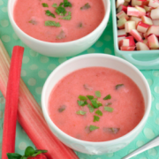 Two bowls of Strawberry Rhubarb Soup displayed with fresh strawberries and rhubarb
