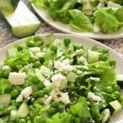 Lettuce bed topped with peas and feta cheese on a plate.