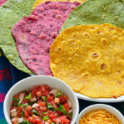 Yellow, red and green tortillas on a platter with salsa and grated cheese on the side.