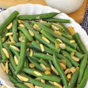 Oval serving dish with tender green beans and toppings. 