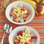 Small bowls of yogurt topped with a cereal and a colorful fruit combination. 