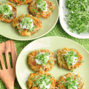 Plate of vegetable and potato patties served with a creamy sauce and microgreens on top.