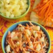 Bowl of shredded carrots with pineapples and raisins in a yogurt dressing.