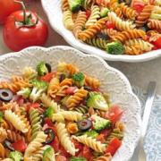 Bowls of colorful spiral pasta with olives and broccoli. 