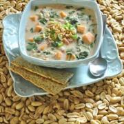 Medium bowl of vegetable and peanut soup on a plate served with crackers.