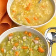 Two bowls of green and yellow pea and vegetable soup.