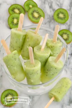 Kiwi popsicles in a bowl sitting on a table with slices of kiwi surrounding.
