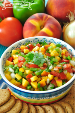 Tazón pequeño de una colorida salsa de durazno y verduras exhibida con galletas saladas.