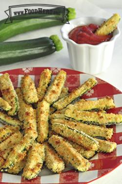 Breaded and baked zucchini slices are shown on a serving platter with a side of marinara sauce.