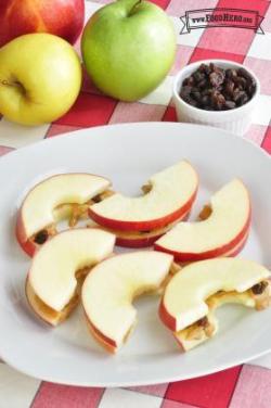 Crispy apple slices with peanut butter and raisin filling are shown on a plate.