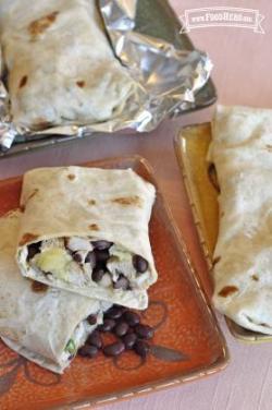 Bean and chicken mix wrapped in flour tortillas and tin foil shown on plates.