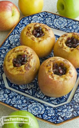 Four cored apples filled with cranberries, butter and brown sugar are baked, broiled and displayed on a serving plate.