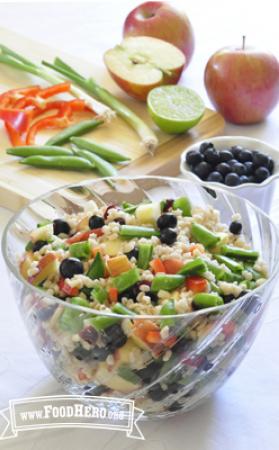 A clear bowl displays a colorful salad of cooked barley, blueberries and crunchy vegetables.