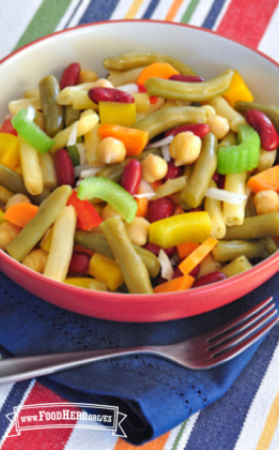 Se muestra un tazón de ensalada elaborada con distintos tipos de frijoles y verduras crujientes sobre un mantel a rayas.