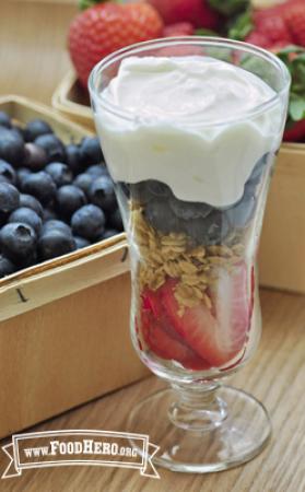 A sundae glass filled with layers of sliced strawberries, granola, blueberries and creamy yogurt.