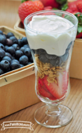 Un vaso de helado lleno de capas de fresas rebanadas, granola, arándanos azules y yogur cremoso.