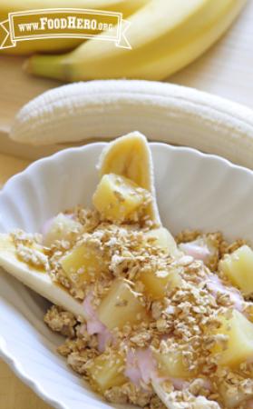 A bowl with halved banana is topped with yogurt, pineapple chunks and a sprinkle of granola.